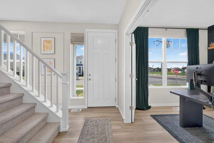 Wood-finish flooring throughout, white paneled entry door, and a staircase with carpeted treads