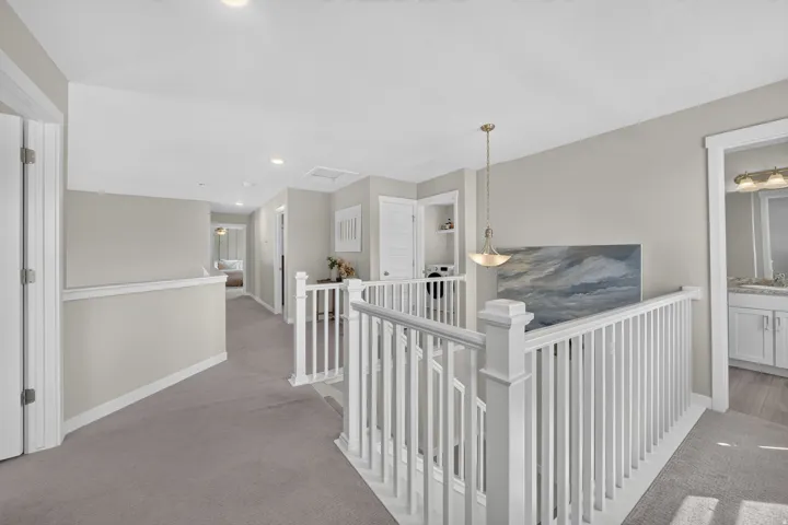 Upper-level hallway featuring a white balustrade, recessed lighting, and carpet flooring