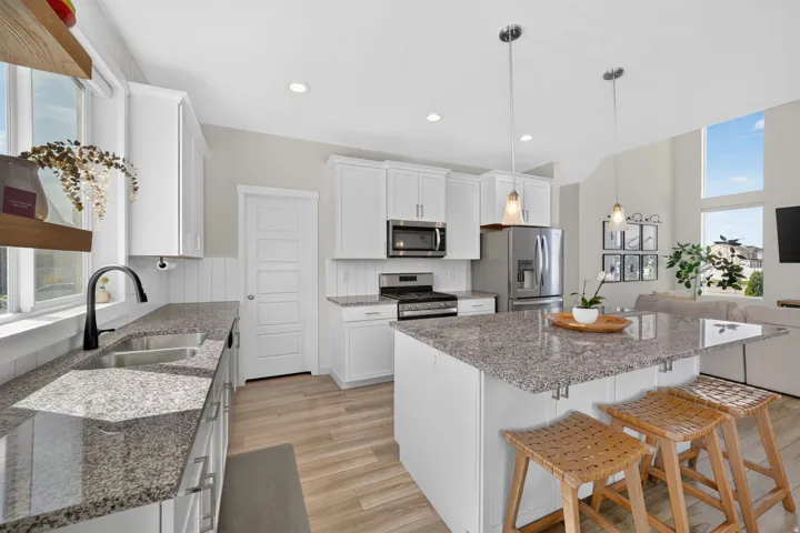 White cabinetry with stainless steel appliances, granite countertops, wood-finish flooring, and a kitchen island with pendant lighting
