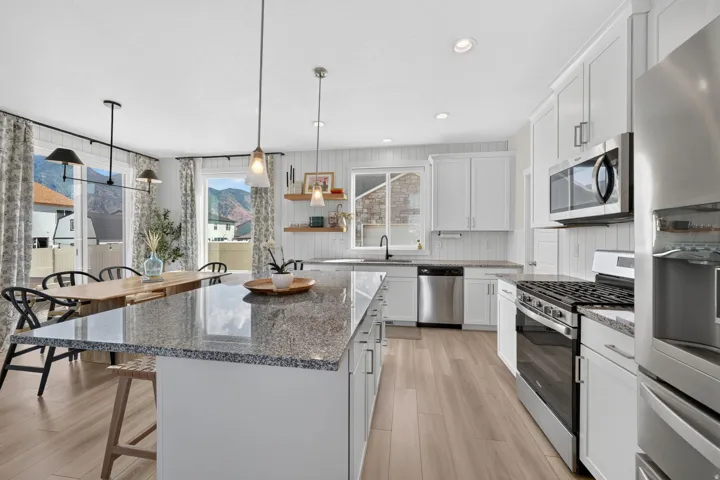 Kitchen with granite countertops, stainless steel appliances, white cabinetry, wood-finish flooring, and recessed lighting