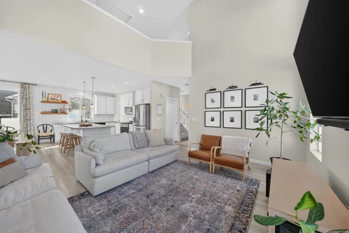 Vaulted ceiling with recessed lighting, wood-finish flooring, kitchen island with seating, stainless steel appliances, and white cabinetry