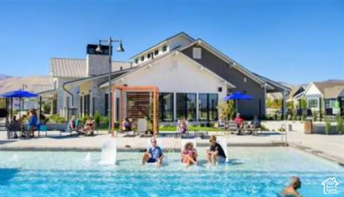 Swimming pool featuring a Baja shelf, surrounding concrete hardscaping, wood-slat pergola, and clubhouse building with white vertical siding and brick masonry accents