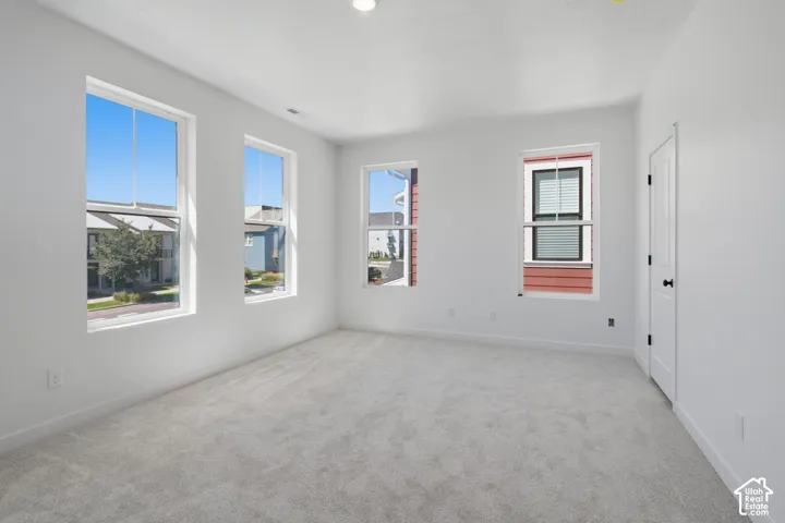 Spacious, primary room with light gray carpet flooring and multiple windows