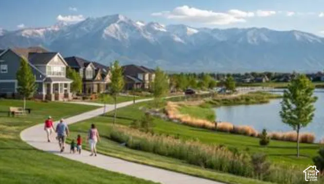 Paved walking and biking paths winding through landscaped green space, adjacent to a waterfront and mountain range