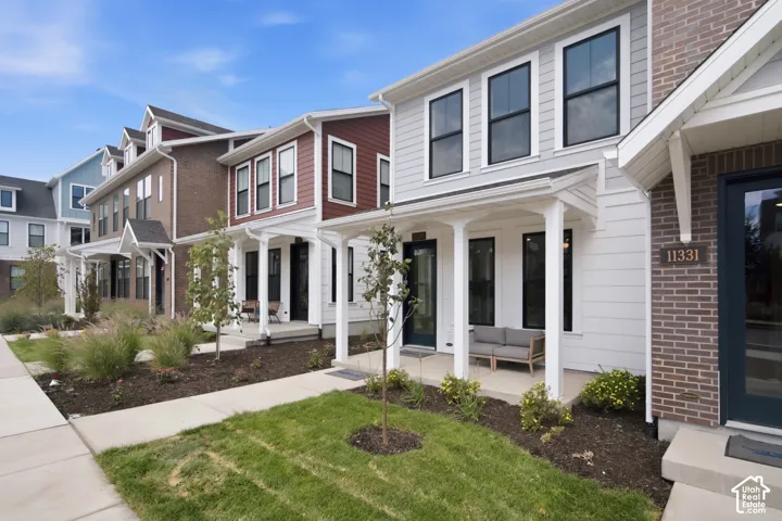 Contemporary exterior featuring large, covered front porch, light grey siding, brick accents, black-framed windows, a covered front porch, and established landscaping