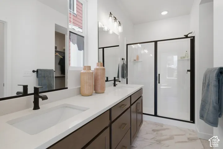 Primary bathroom featuring dougnle vanity with undermount sinks and matte black fixtures, white countertop, dark wood-finish cabinetry, and a glass-enclosed shower with black framing