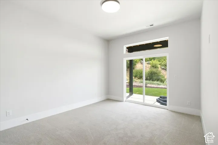 Neutral-toned carpeting, white walls, modern ceiling light fixture, white sliding glass door, and backyard access