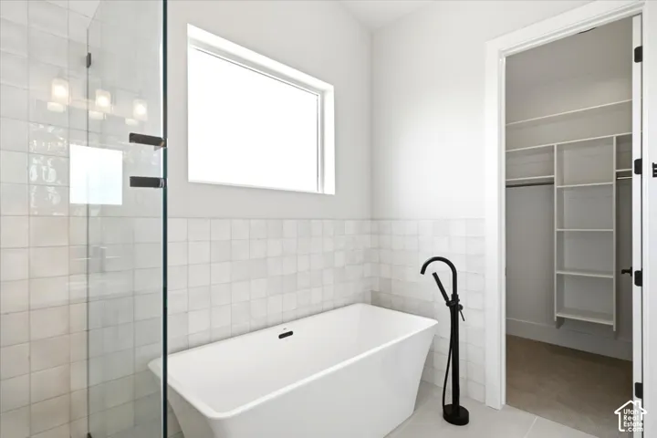 Freestanding soaking tub with matte black floor-mounted faucet, glass-enclosed shower, transom window, and white square wall tiling