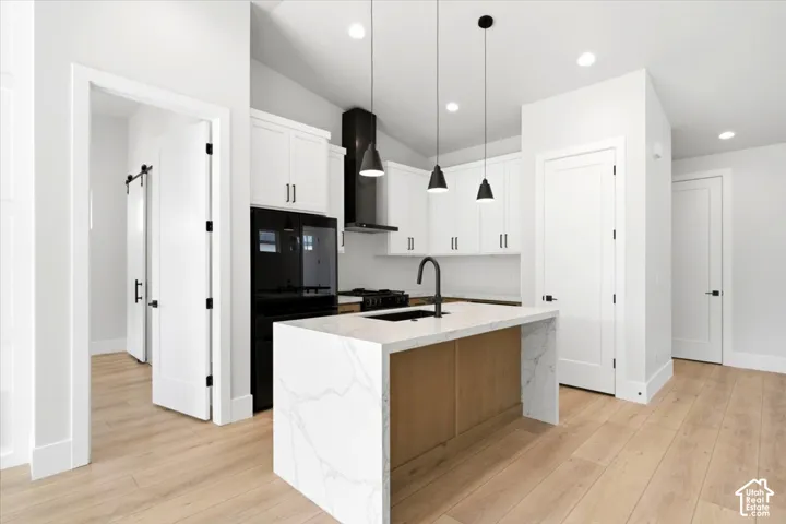 Kitchen featuring white cabinetry, a waterfall island with stone-finish countertop, black appliances, and wood-finish flooring