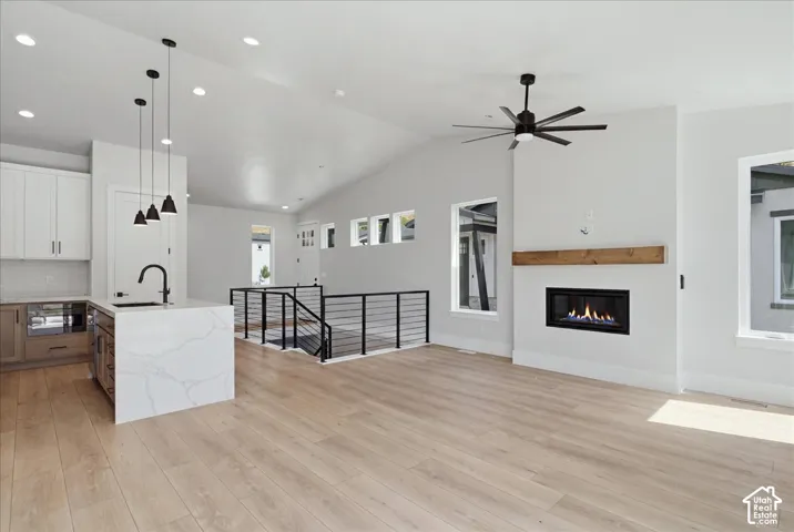 Vaulted ceilings with recessed lighting, wood-finish flooring, a contemporary fireplace with a wood mantle, and a kitchen island with stone countertops
