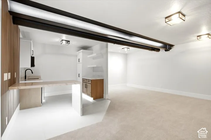 Wet bar featuring a rectangular sink with a matte black faucet, wood-finish cabinetry, and light-toned countertop