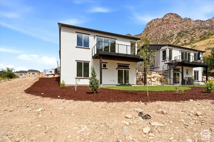 Modern exterior featuring a balcony with black metal railings, a ground-level patio door, a spiral staircase, and an expansive mountain backdrop