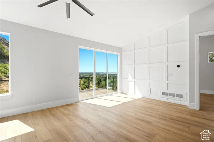 Vaulted ceiling with a contemporary ceiling fan, wood-finish flooring, and a decorative paneled accent wall