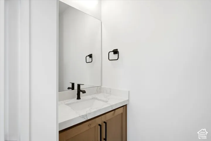 Vanity with a light wood-finish base, white countertop with veining, rectangular undermount sink, and matte black faucet