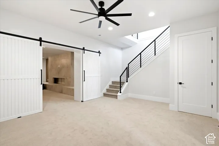 Neutral-toned carpeting, modern black ceiling fan, white barn doors, contemporary staircase with black railing, and recessed lighting