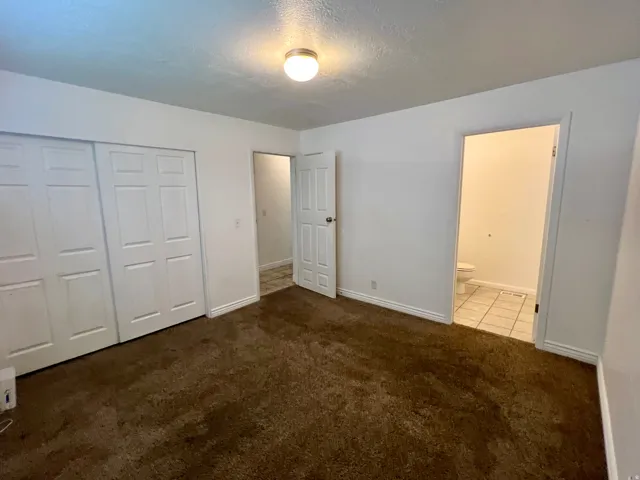 Carpeted owner's bedroom featuring white bi-fold closet doors, a flush mount ceiling light, and an entry to a  private bathroom.