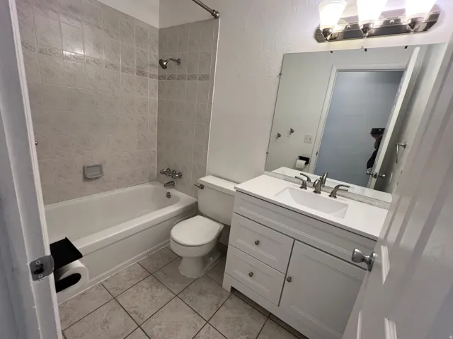 Tiled bathtub with shower, white vanity with integrated sink, and an overhead vanity light fixture