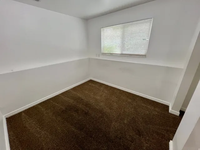 Brown carpeted flooring with white wall finishes and a window with horizontal blinds