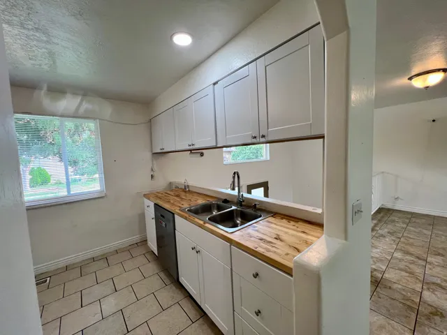 White cabinetry with brushed nickel hardware, wood-finish countertops, stainless steel double basin sink, and tile flooring