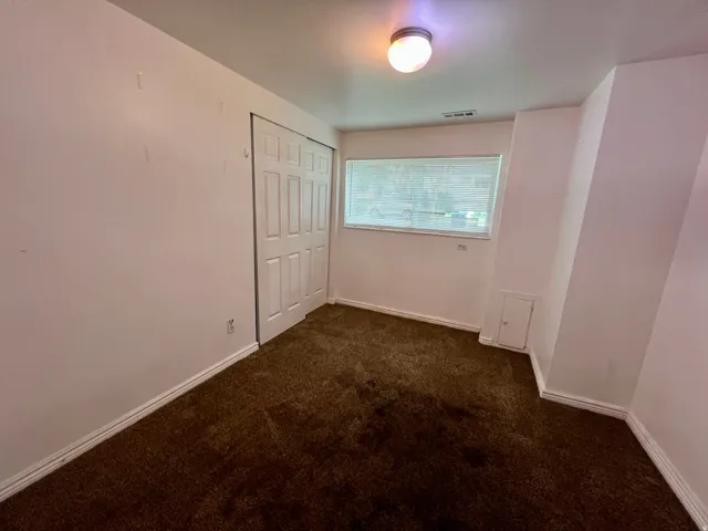 Wall-to-wall carpeting, sliding panel closet doors, ceiling-mounted light fixture, and a single window with blinds