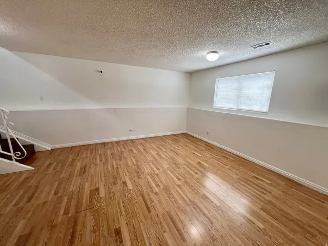Wood-finish flooring with white wall finishes and a window featuring horizontal blinds