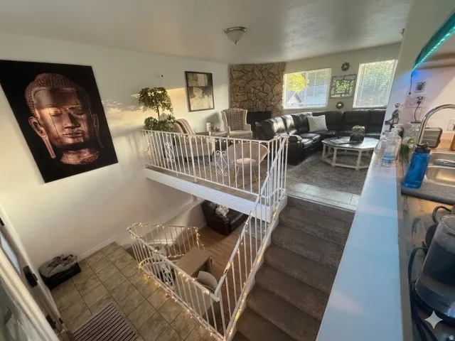 Split-level living area featuring a white metal railing, carpeted stairs, and a tiled entryway