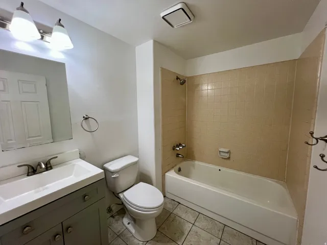 Bathroom with a vanity featuring a single basin sink, a toilet, a bathtub with tiled surround, and tiled flooring