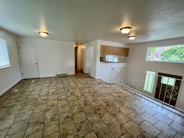 Tile flooring throughout, white interior walls, overhead lighting, kitchen pass-through, and a decorative staircase railing