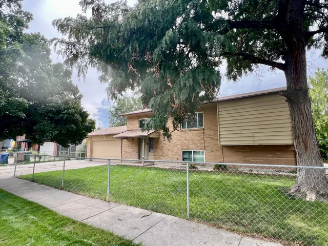 Charming brick and siding residence featuring a spacious front lawn with mature shade trees, chain-link perimeter fencing, and established landscaping