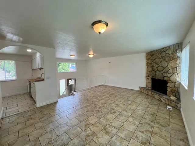 Stone-surround fireplace with hearth, tiled flooring, white cabinetry, archway entry, and ceiling-mounted lighting fixtures