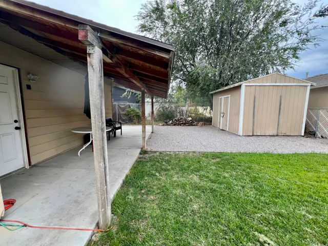 Covered patio with a concrete surface, expansive lawn, gravel area, and a detached storage shed
