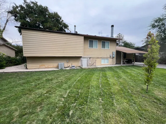 Expansive backyard featuring a manicured lawn, an extended covered patio, mature perimeter trees, and a gravel border with RV or extra parking