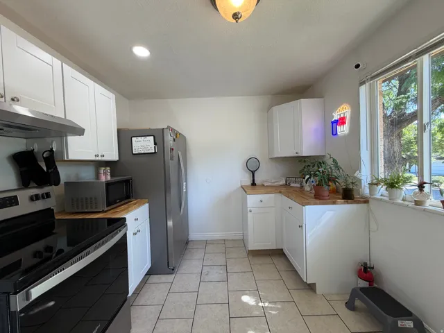 Kitchen featuring stainless steel appliances, wood-finish countertops, white cabinetry, and tile flooring
