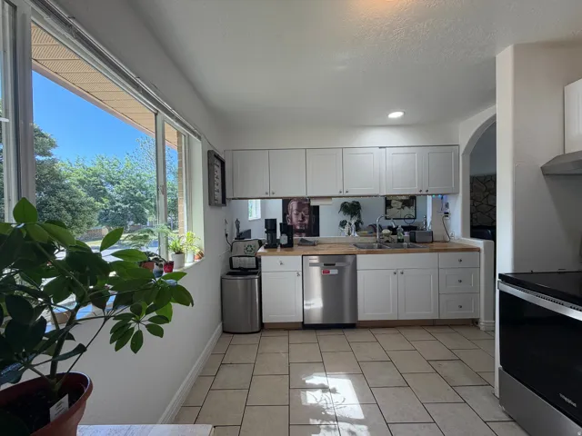 Kitchen featuring a generous window, white cabinetry, wood-finish countertops, stainless steel appliances, and tile flooring