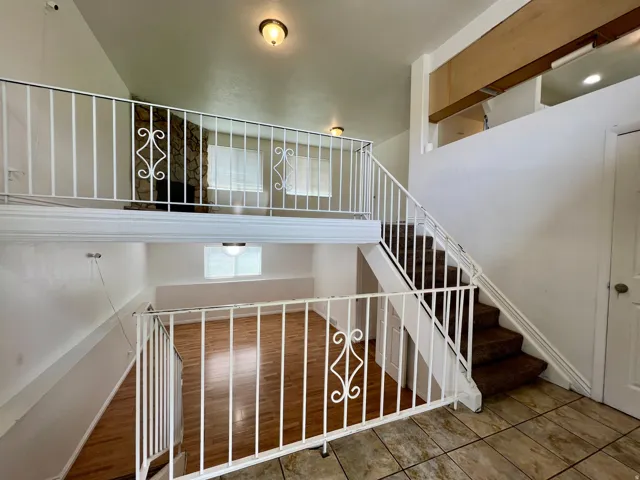 Open-concept interior featuring a lofted area, white decorative railings, a stone fireplace, wood-finish flooring, and a carpeted staircase