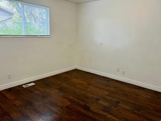 Wood-finish flooring with white trim, a single window, and textured walls