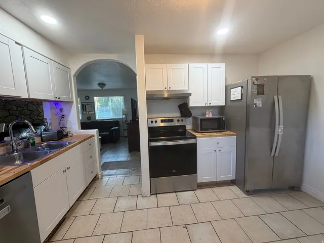 White shaker-style cabinetry, wood-finish countertops, stainless steel appliances, and tile flooring