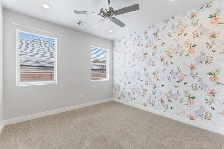 Recessed lighting, ceiling fan, two windows with blinds, patterned accent wall, and neutral carpeting