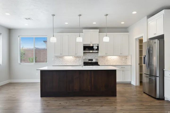 Kitchen with a dark wood-finish island, white cabinetry, integrated stainless steel appliances, pendant lighting, and wood-finish flooring