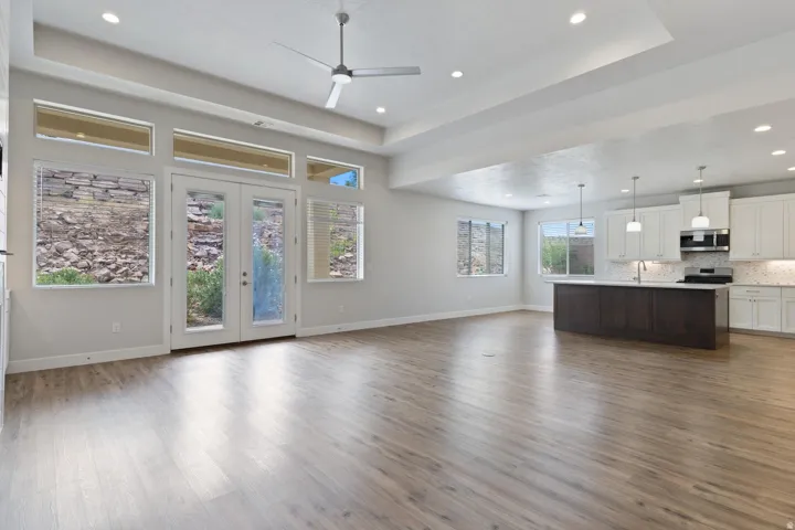 Spacious room featuring wood-finish flooring, a contemporary ceiling fan, recessed lighting, and a white kitchen with a dark-toned island