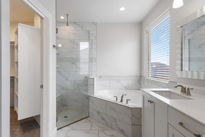 Corner bathtub with tile surround, glass-enclosed shower, single vanity with integrated sink, and built-in closet shelving