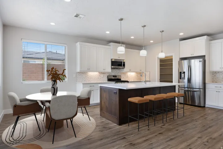 Open-concept kitchen featuring wood-finish flooring, white cabinetry, a large center island with pendant lighting, stainless steel appliances, and a built-in pantry