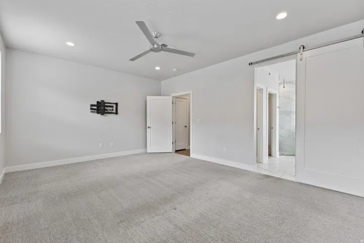 Recessed lighting, ceiling fan, carpet flooring, flat panel interior doors, and a sliding barn door with a metal rail