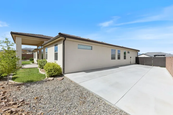 Expansive concrete driveway, stucco exterior, multiple windows, covered patio, and landscaped grounds