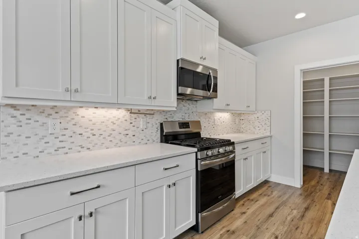 White shaker cabinetry, stainless steel appliances, mosaic tile backsplash, light-toned countertops, and wood-finish flooring