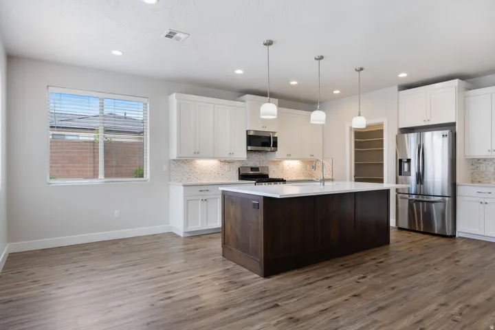 Kitchen featuring wood-finish flooring, a central island with a white countertop, pendant lighting, stainless steel appliances, and white cabinetry with a tile backsplash