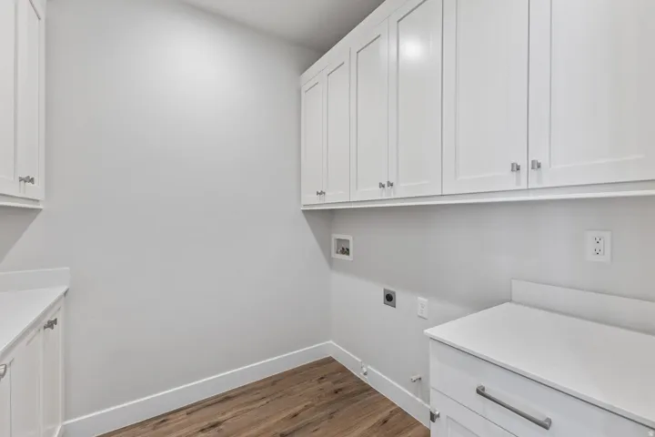 White shaker cabinetry, wood-finish flooring, white countertops, modern hardware, and wall-mounted electrical outlets
