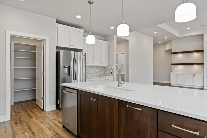 Kitchen featuring white upper cabinetry, dark wood-finish island cabinetry, stainless steel appliances, a large pantry with shelving, and pendant lighting