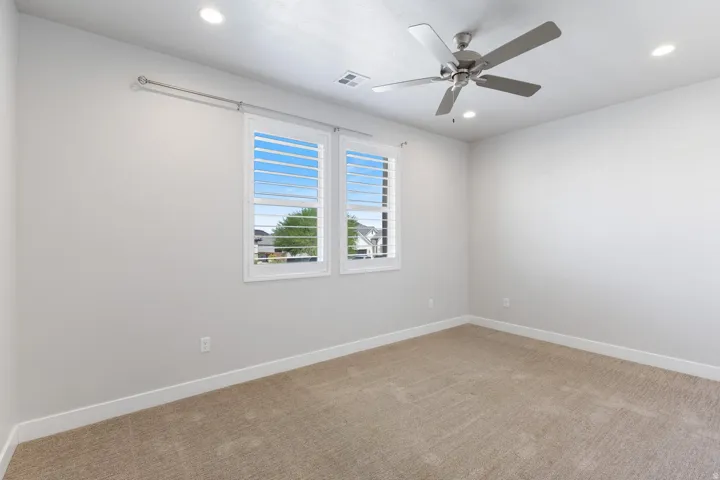 Recessed ceiling lighting, ceiling fan, neutral wall paint, plantation shutters, and carpet flooring