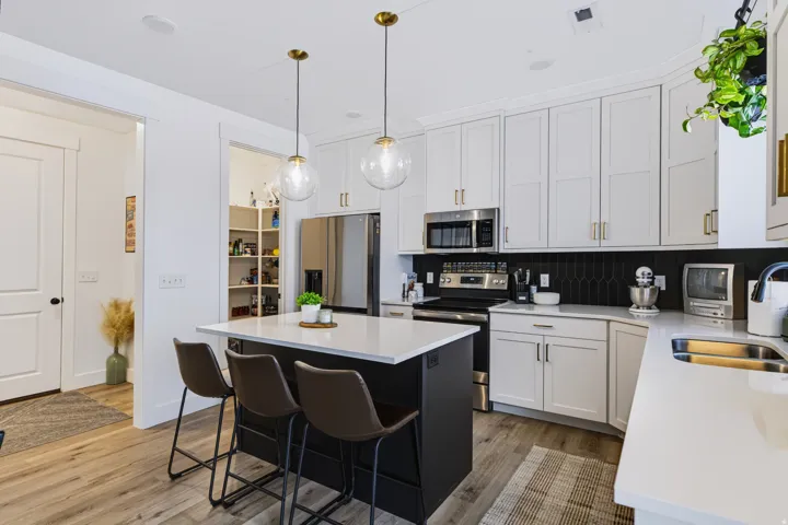 Kitchen featuring wood-finish flooring, white cabinetry, dark island with seating, stainless steel appliances, and a walk-in pantry